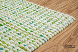 Cashew Loop — Green wool rug shown flat and in full on a plain white ground, seen from a three-quarter angle (first pass)