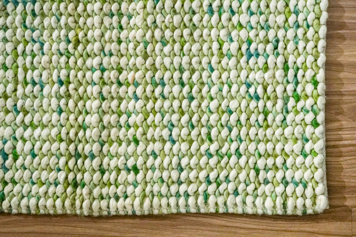 Green Cashew Loop — chunky wool loop rug showing the lower edge and right corner on wood flooring