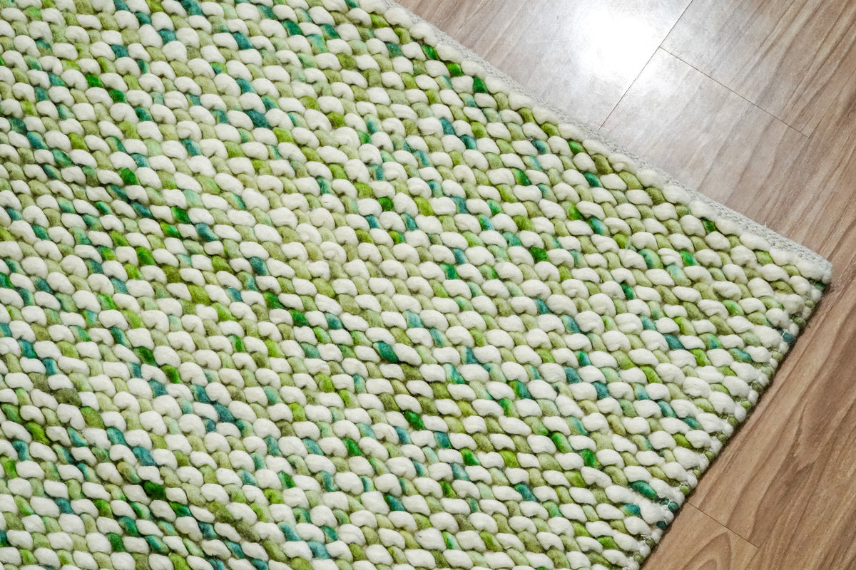 Green Cashew Loop — oblique view across the chunky wool loops toward the far corner on wood flooring