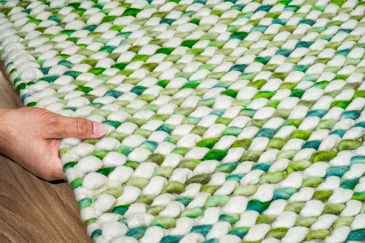 Green Cashew Loop — hand holding the rug edge to display the chunky wool loop surface