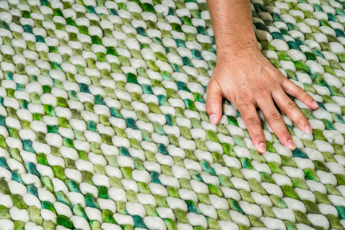 Cashew Loop — hand resting on the green and ivory chunky wool loops to show their visible scale