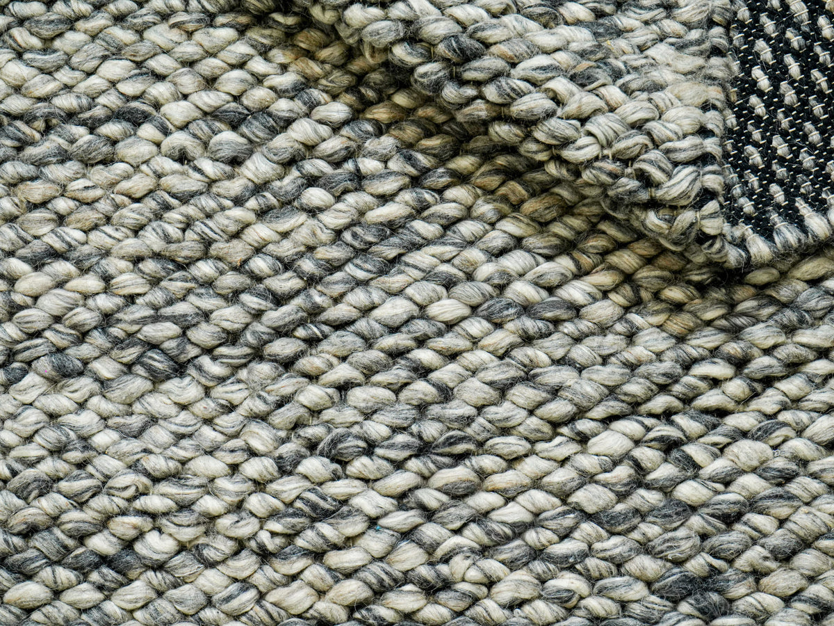 Gray Cashew Loops — Wool rug with a loose fold across the surface and underside visible at the upper right