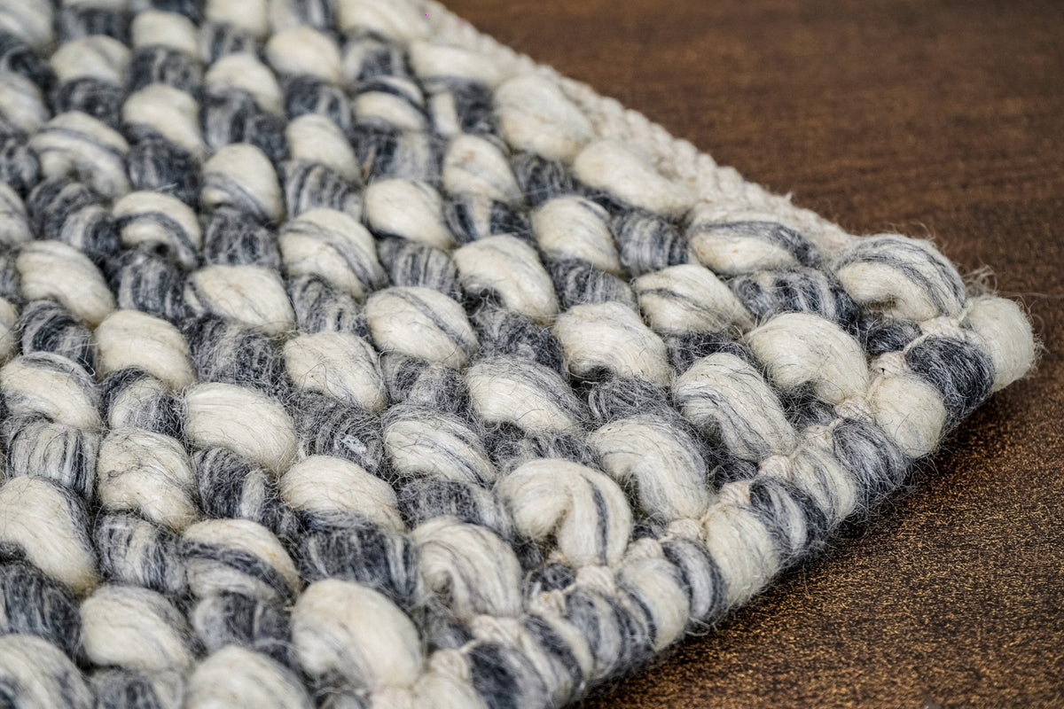 Cashew Loops — Wool rug corner detail with pale and dark gray loops and a rounded edge