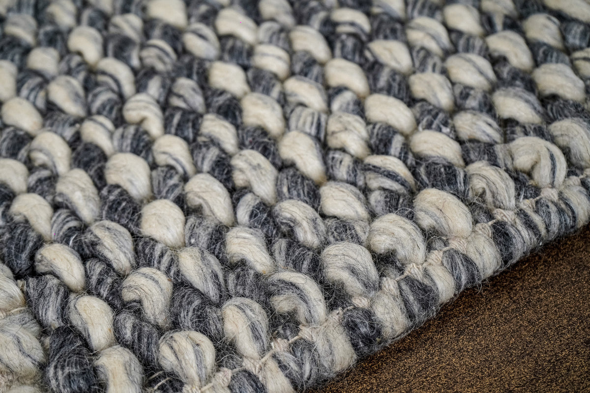 Gray Cashew Loops — Wool rug diagonal edge view with dense loops beside a brown surface