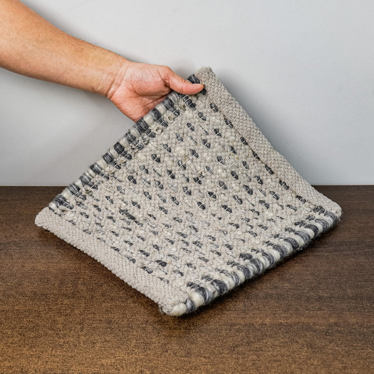 Gray Cashew Loops — Wool rug underside lifted by hand, showing the woven reverse and finished edges