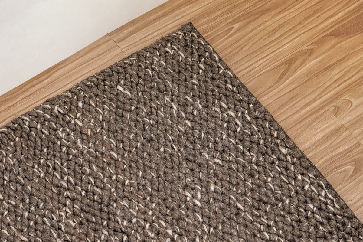 Cashew Loops — angled view of the brown wool rug's corner beside a wall and wood floor