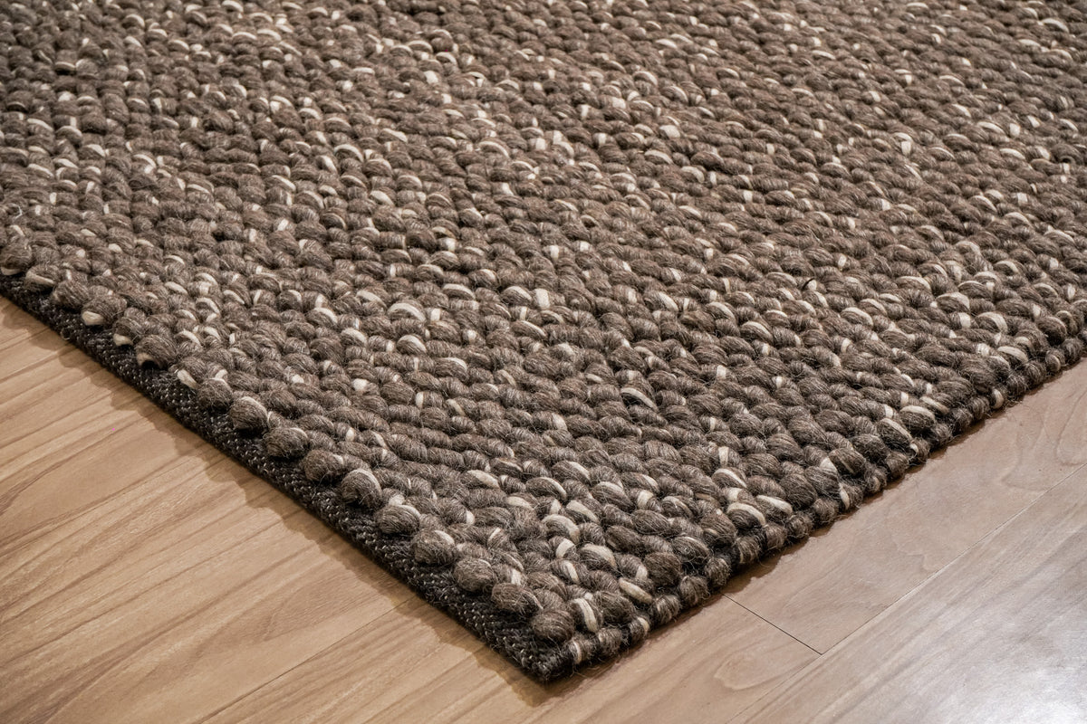 Cashew Loops — low angled view of a brown wool rug corner showing chunky loops and dark edge binding