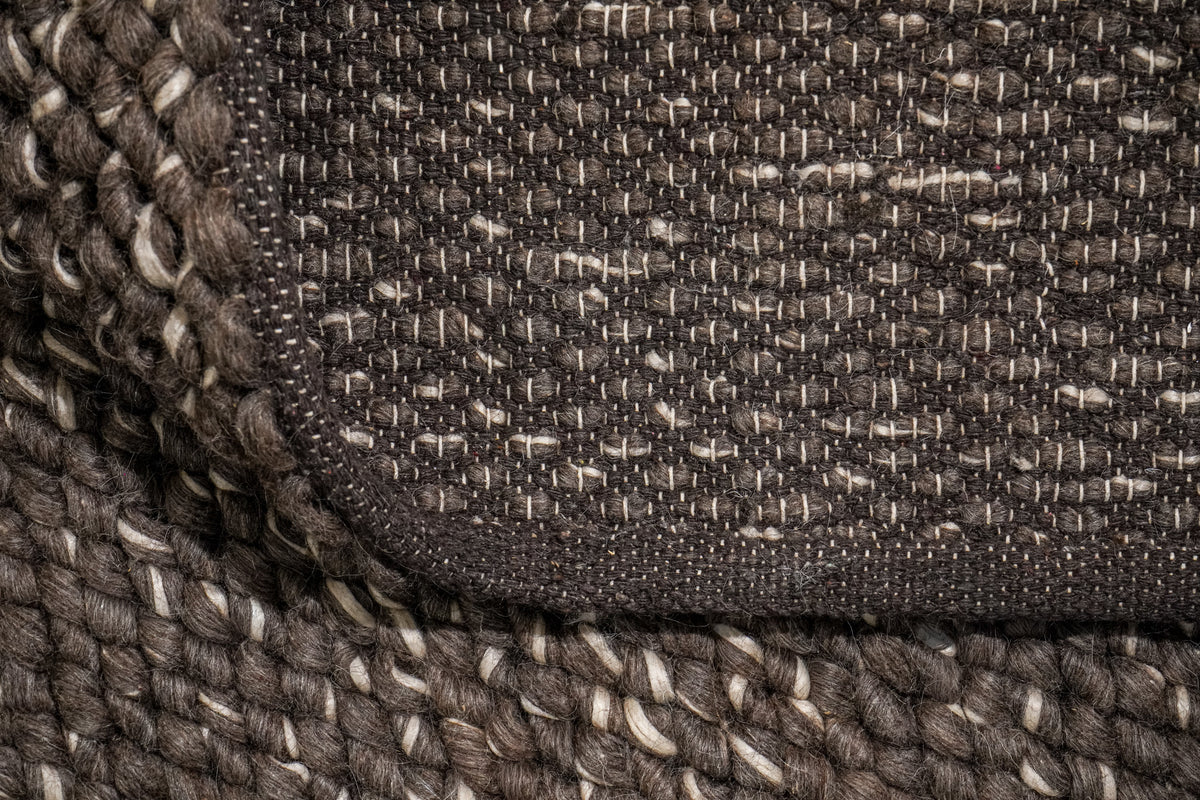 Cashew Loops — turned-back corner showing the brown wool rug's woven reverse and dark finished border