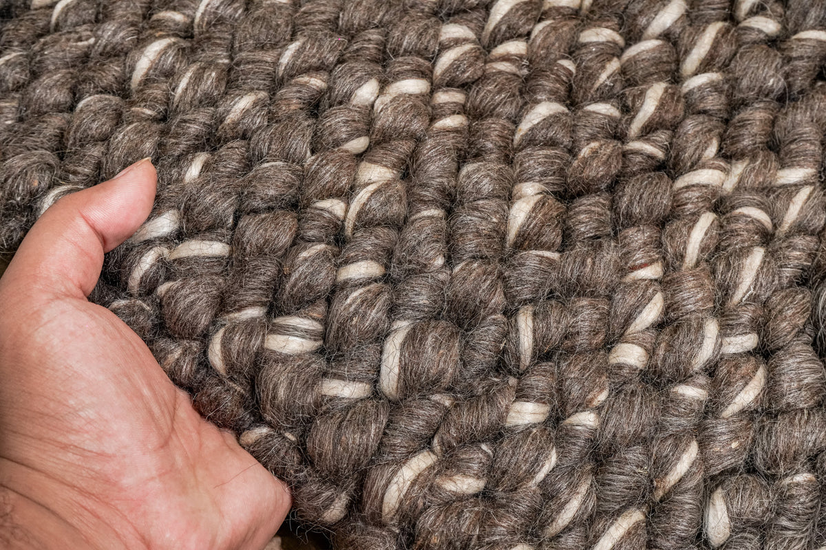 Cashew Loops — hand lifting the brown wool rug to show its chunky loops and ivory strands