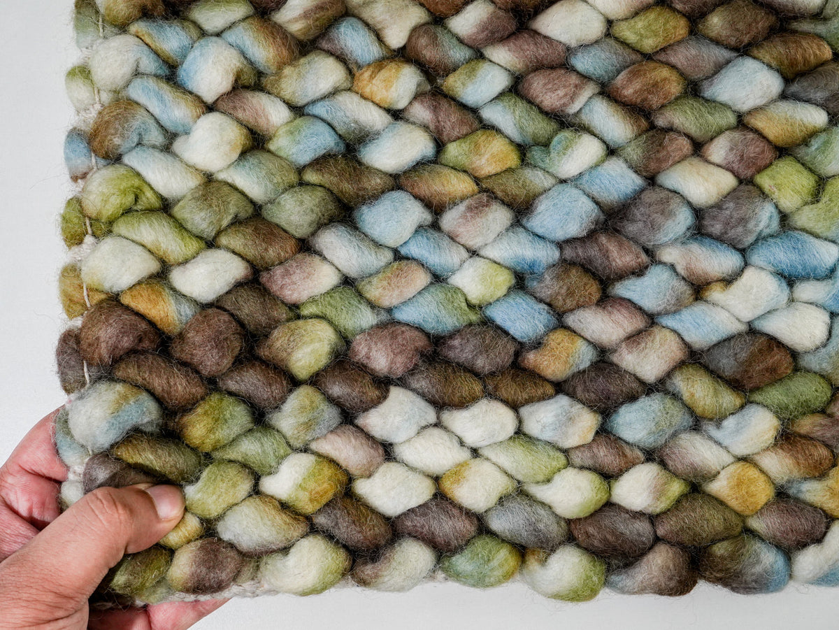 Multicolor Cashew Loop — Wool rug front held at the lower left corner against a white background