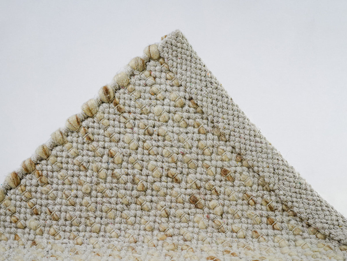 Beige Cashew Loop — Wool rug, raised underside corner showing the woven edge band