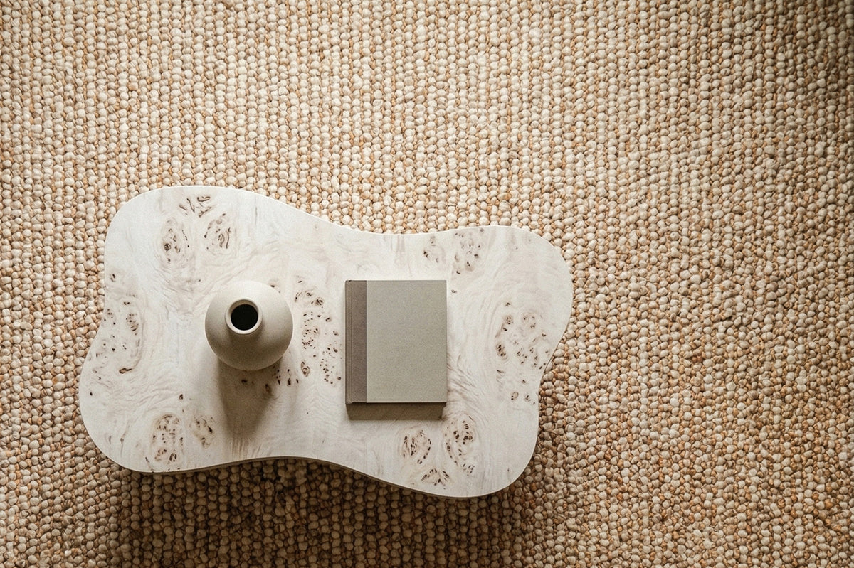 Loops With Jute — Beige Wool rug seen overhead with a curved coffee table, vase and book