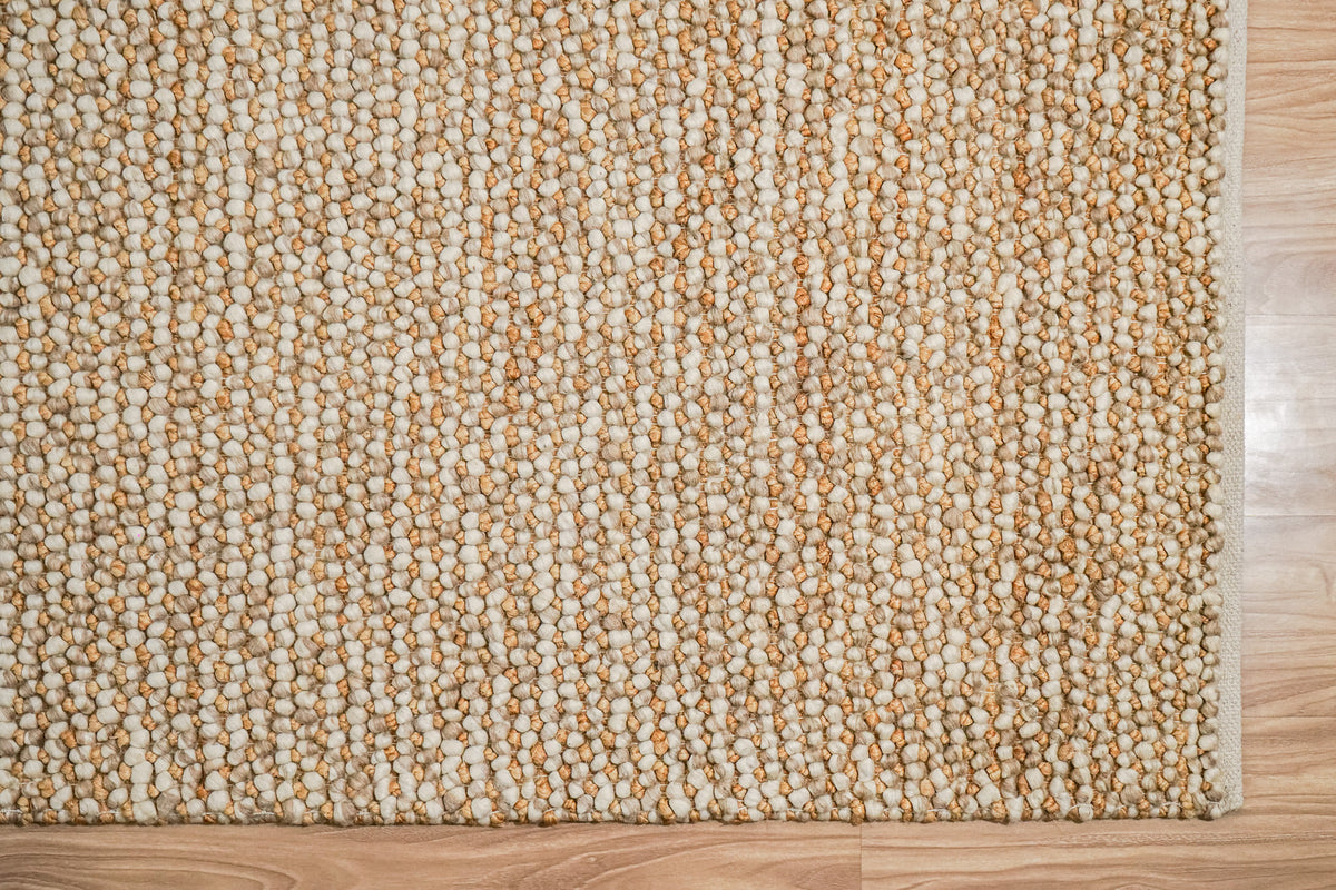 Loops With Jute — Beige Wool rug viewed overhead with its lower and right edges visible against a wood floor