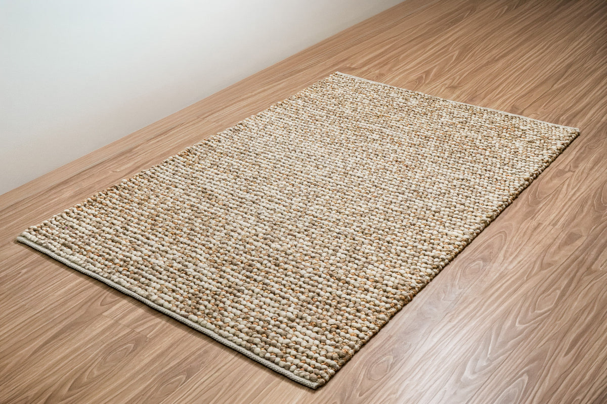 Loops With Jute — Beige Wool rug shown in full at an angle beside a plain wall