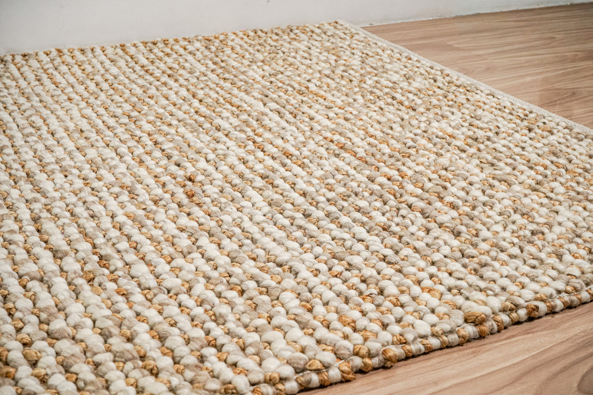 Loops With Jute — Beige Wool rug viewed across its textured surface toward a wall, with the front edge on a wood floor