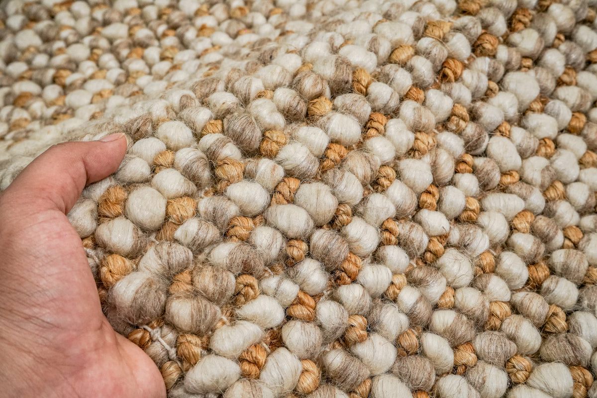 Loops With Jute — Beige Wool rug lifted by a hand to show the chunky loop surface in close-up