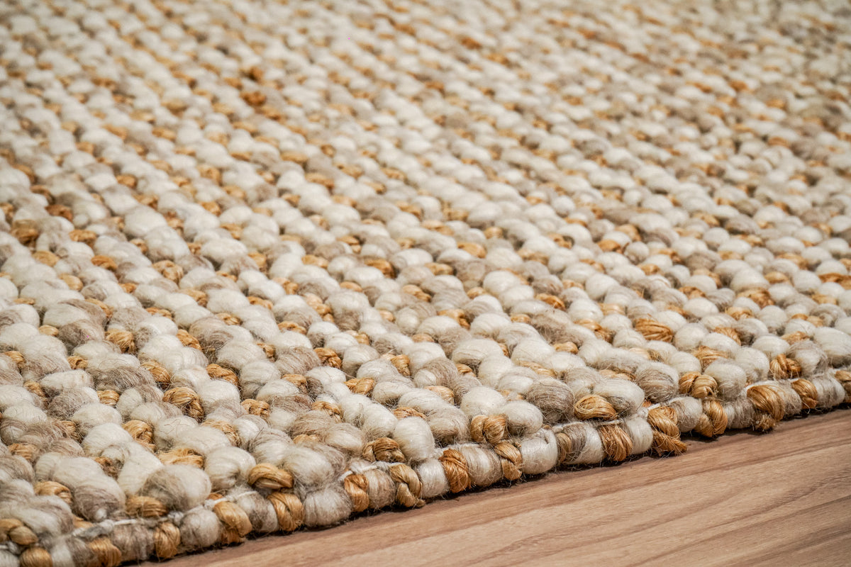 Loops With Jute — Beige Wool rug in an angled close-up of rounded loops along the edge on a wood floor