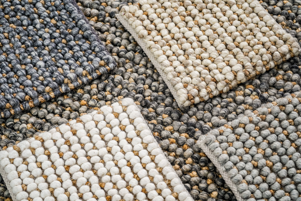 Loops With Jute — ivory wool rug sample at the bottom of a layered stack beside a hand lifting an upper sample