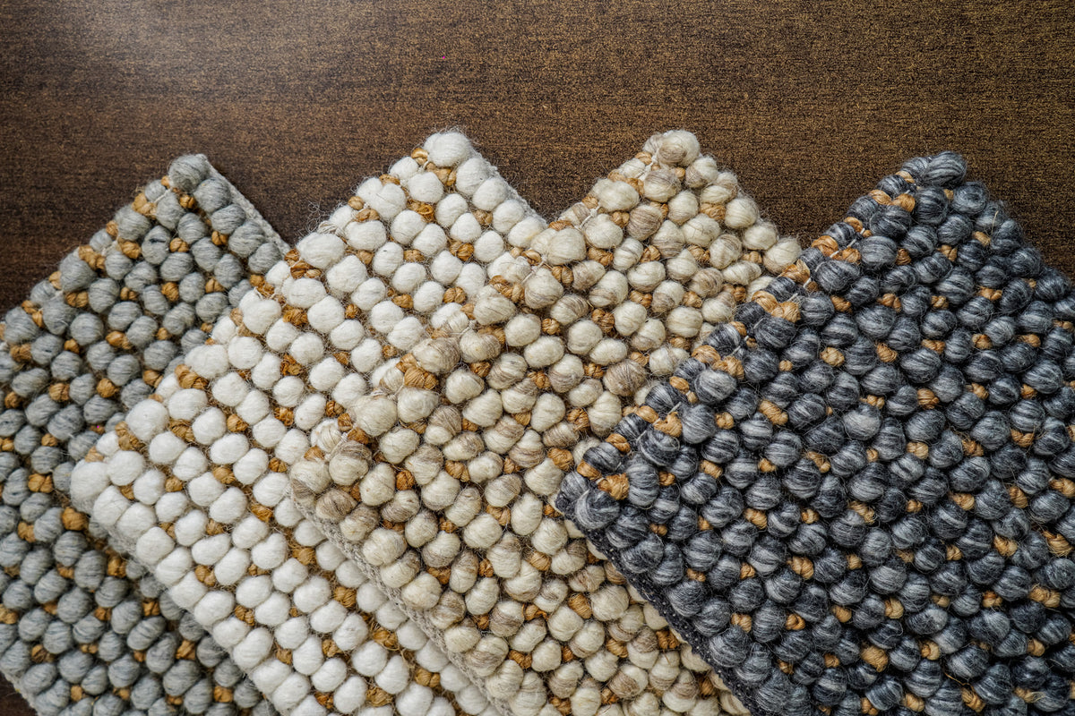 Loops With Jute — gray wool rug sample at the left of a fan-shaped arrangement on a brown surface