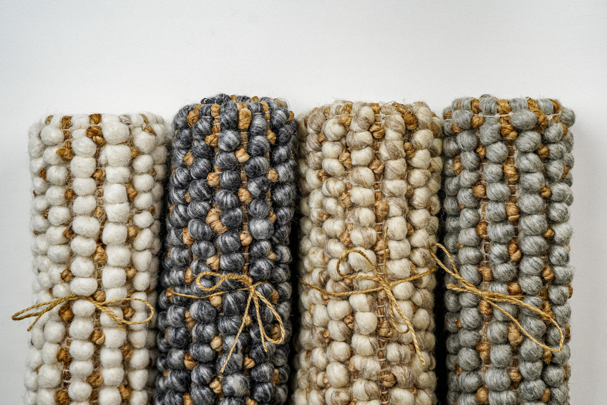 Loops With Jute — gray wool rug sample standing rolled and tied at the right of a lineup