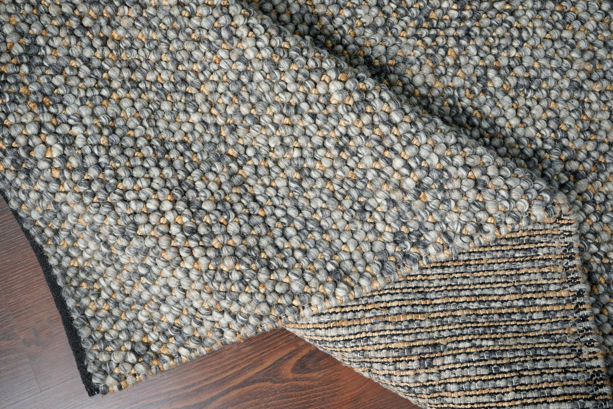 Loops With Jute — Gray Wool rug folded back to show the striped underside and dark edge on a wood floor