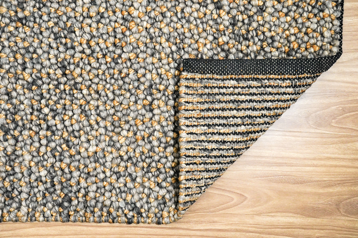 Loops With Jute — Gray Wool rug viewed overhead with one corner folded back to show the underside and bound edge