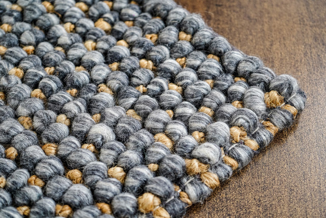 Loops With Jute — close-up of the gray wool rug's weave, rounded loop pile and edge finish on a wood surface