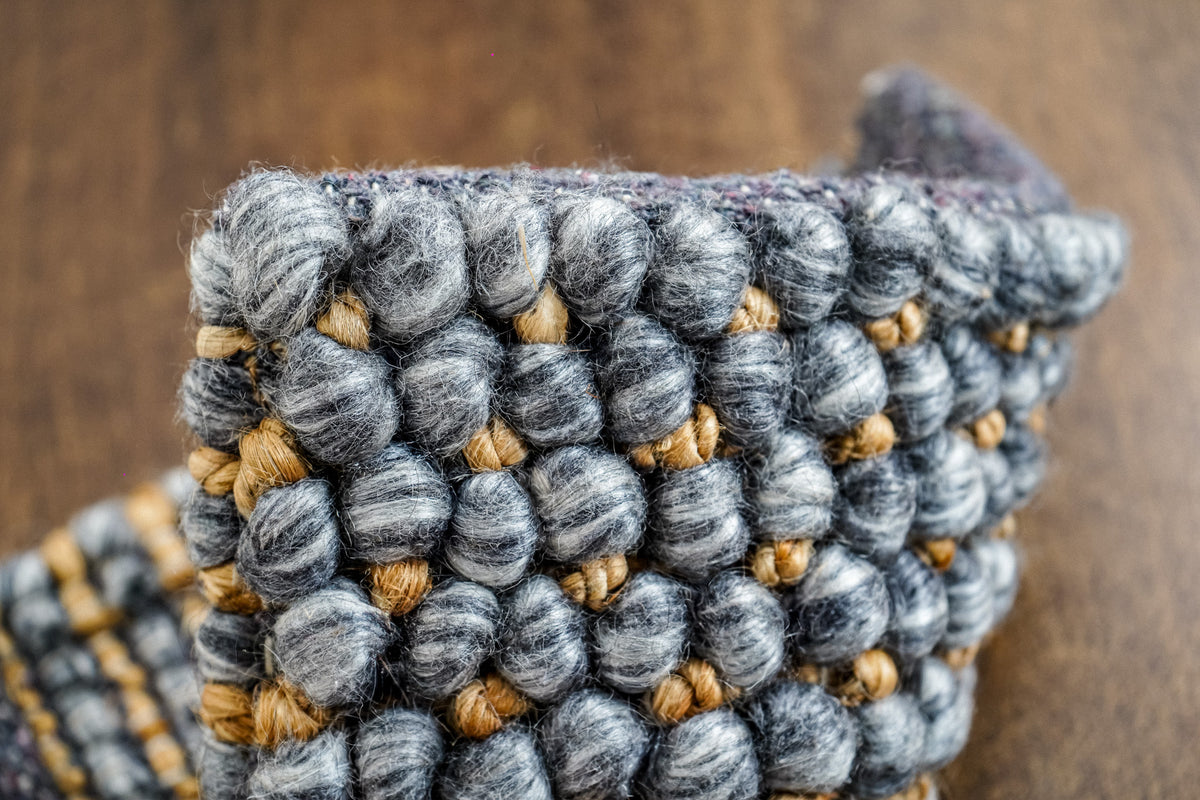 Loops With Jute — gray wool rug sample folded upright, showing rounded loops and golden-toned accents