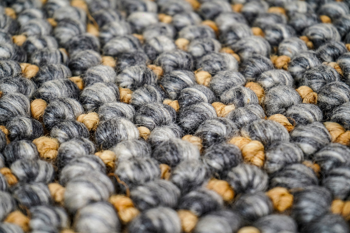 Loops With Jute — macro view of the gray wool rug's mottled loops and small golden-toned accents