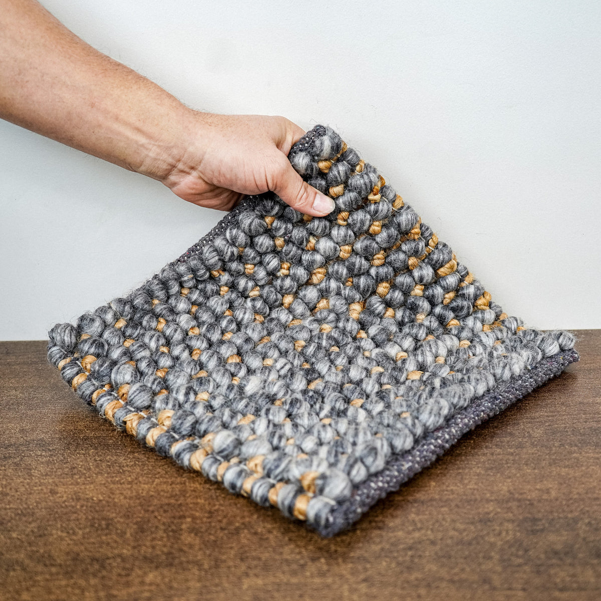 Loops With Jute — gray wool rug sample lifted by hand to show its textured face and drape