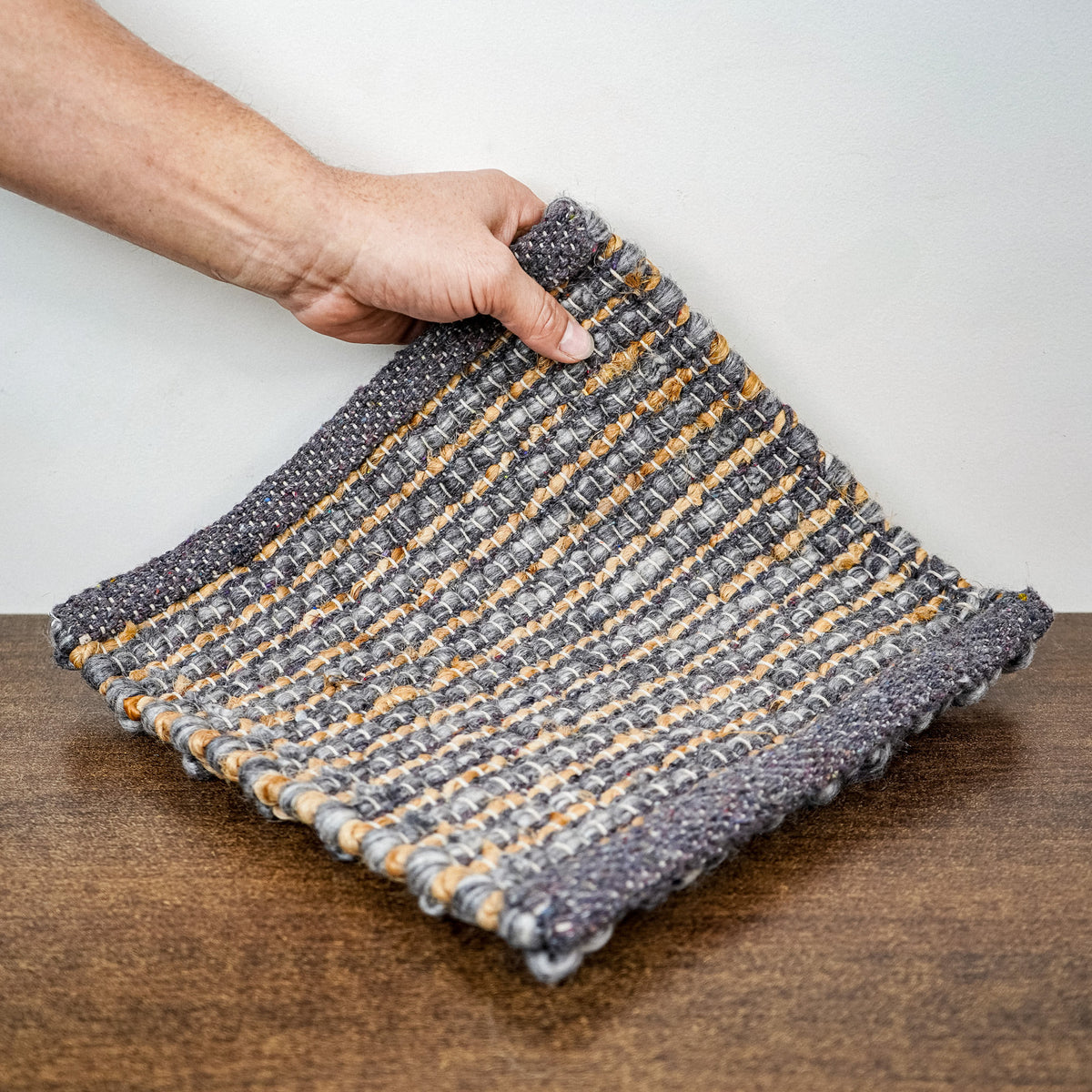 Loops With Jute — gray wool rug sample lifted by hand to reveal the underside and finished edges