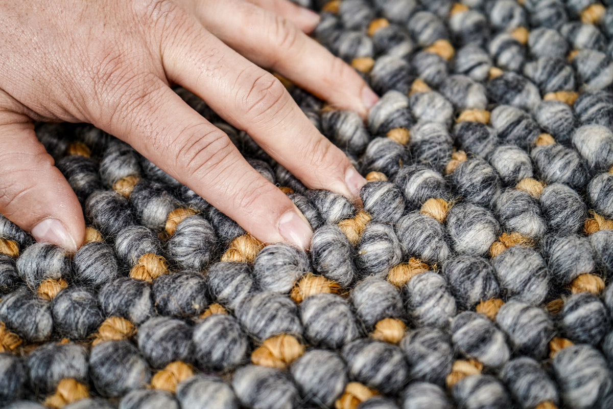 Loops With Jute — hand pressing into the gray wool rug's rounded loop surface