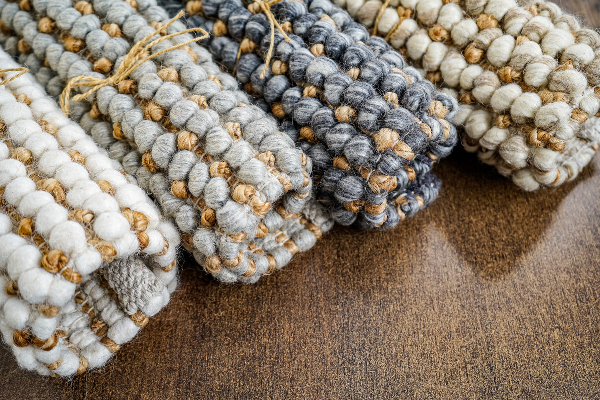 Loops With Jute — gray wool rug sample rolled near the center, with its curled edge visible on wood