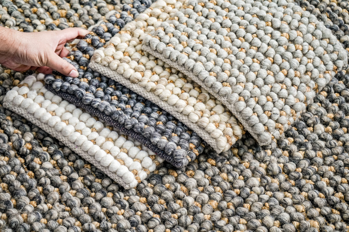 Loops With Jute — hand lifting the gray wool rug sample within a stack of textured samples