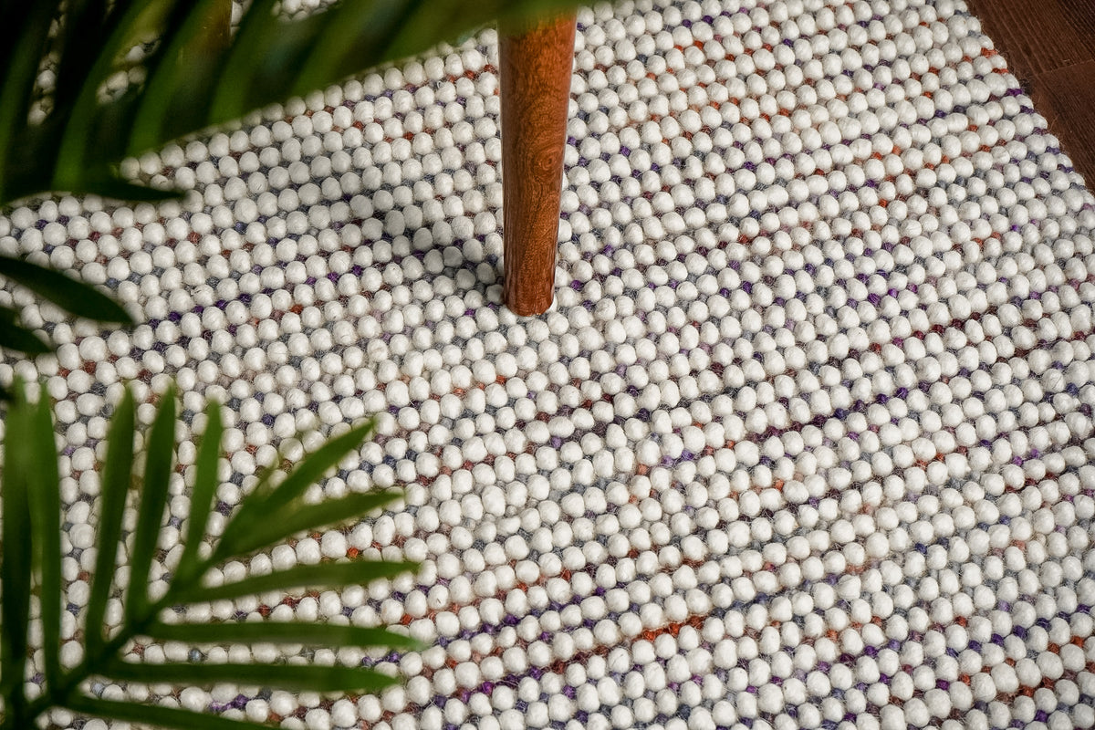 Alter Loops — Purple Wool rug styled in a living room, with a wooden furniture leg and green leaves above the rounded ivory…