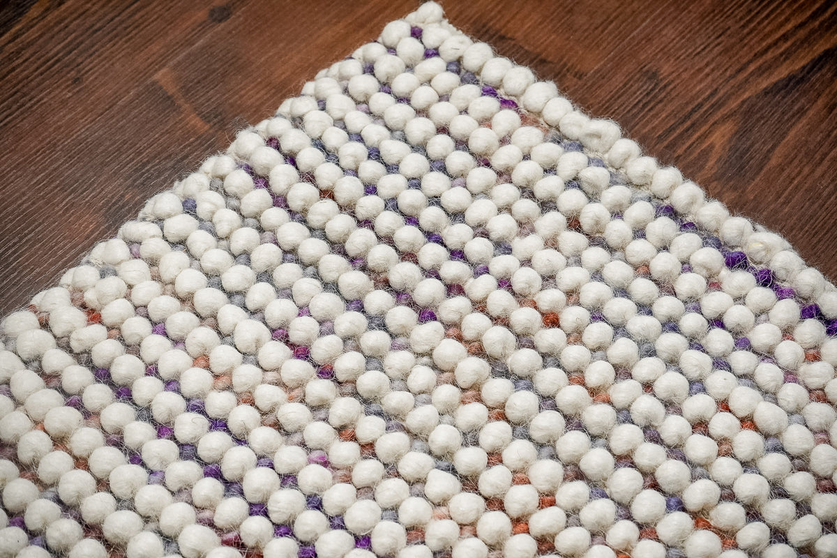 Alter Loops — Purple Wool rug corner viewed diagonally on a brown wood floor, showing rows of rounded loops