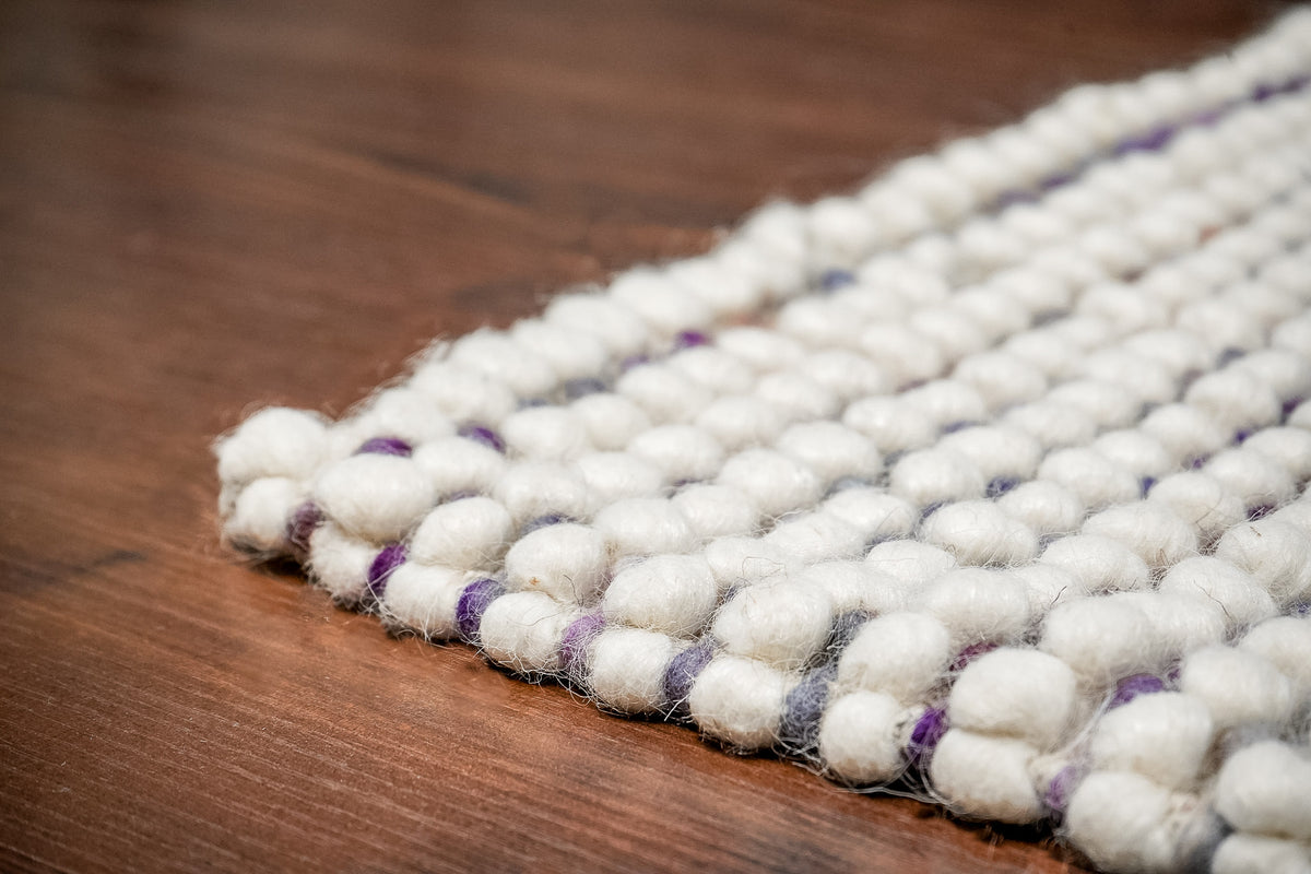 Alter Loops — Purple Wool rug edge viewed at floor level, with raised ivory loops and purple details