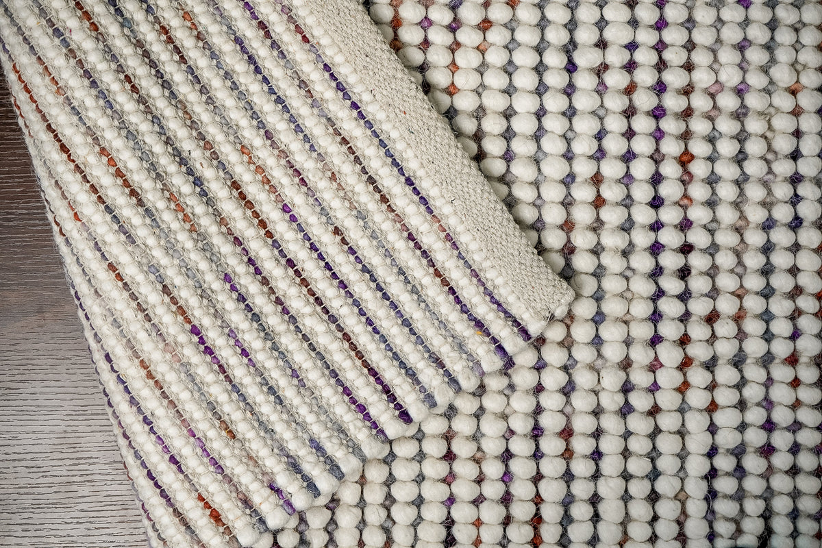 Alter Loops — Purple Wool rug folded back to show the striped woven reverse and a broad ivory edge band