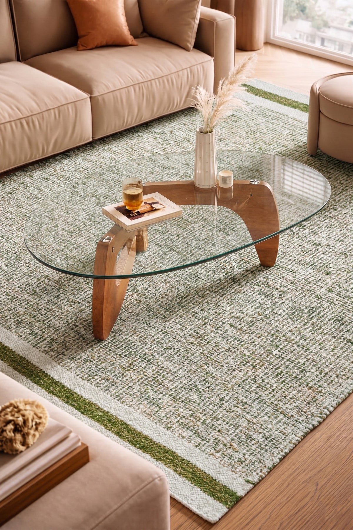Green wool rug beneath an oval glass coffee table between tan seating, showing pale bands and a green end stripe.