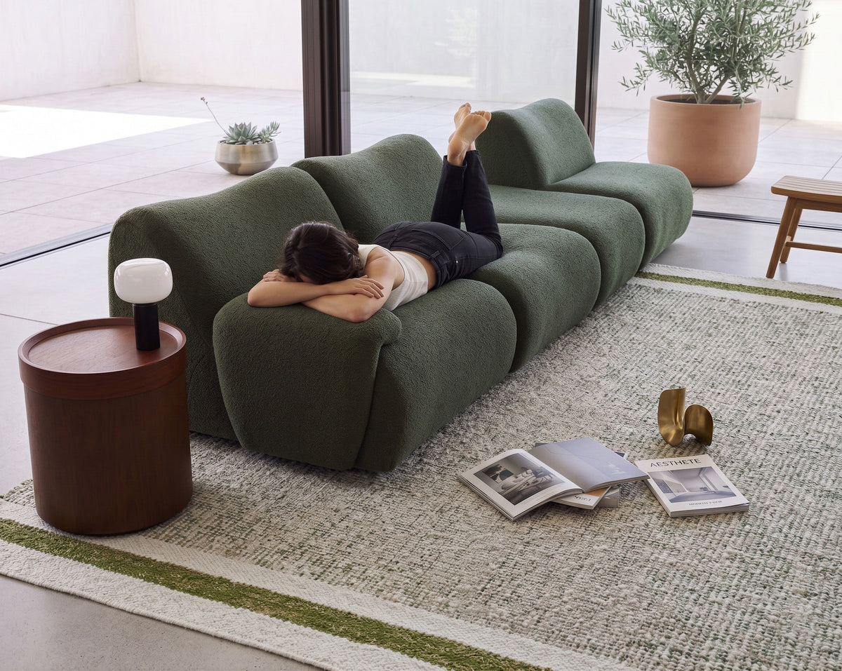 Green wool rug with a broad pale end band and green stripe beside a dark green sofa with a person reclining.