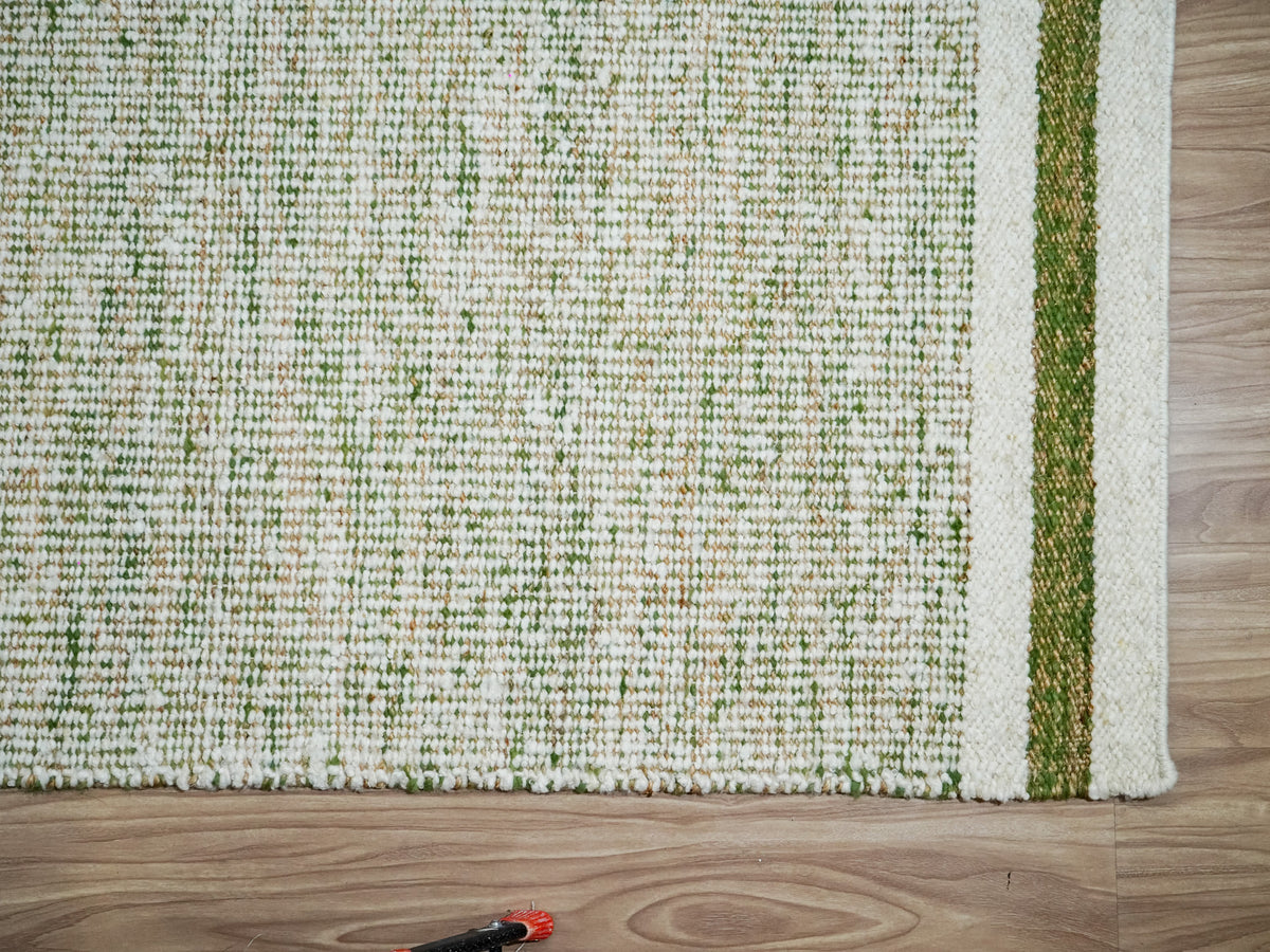 Green wool rug end on a wood floor, showing the pale border, green stripe and a small red and black object below.