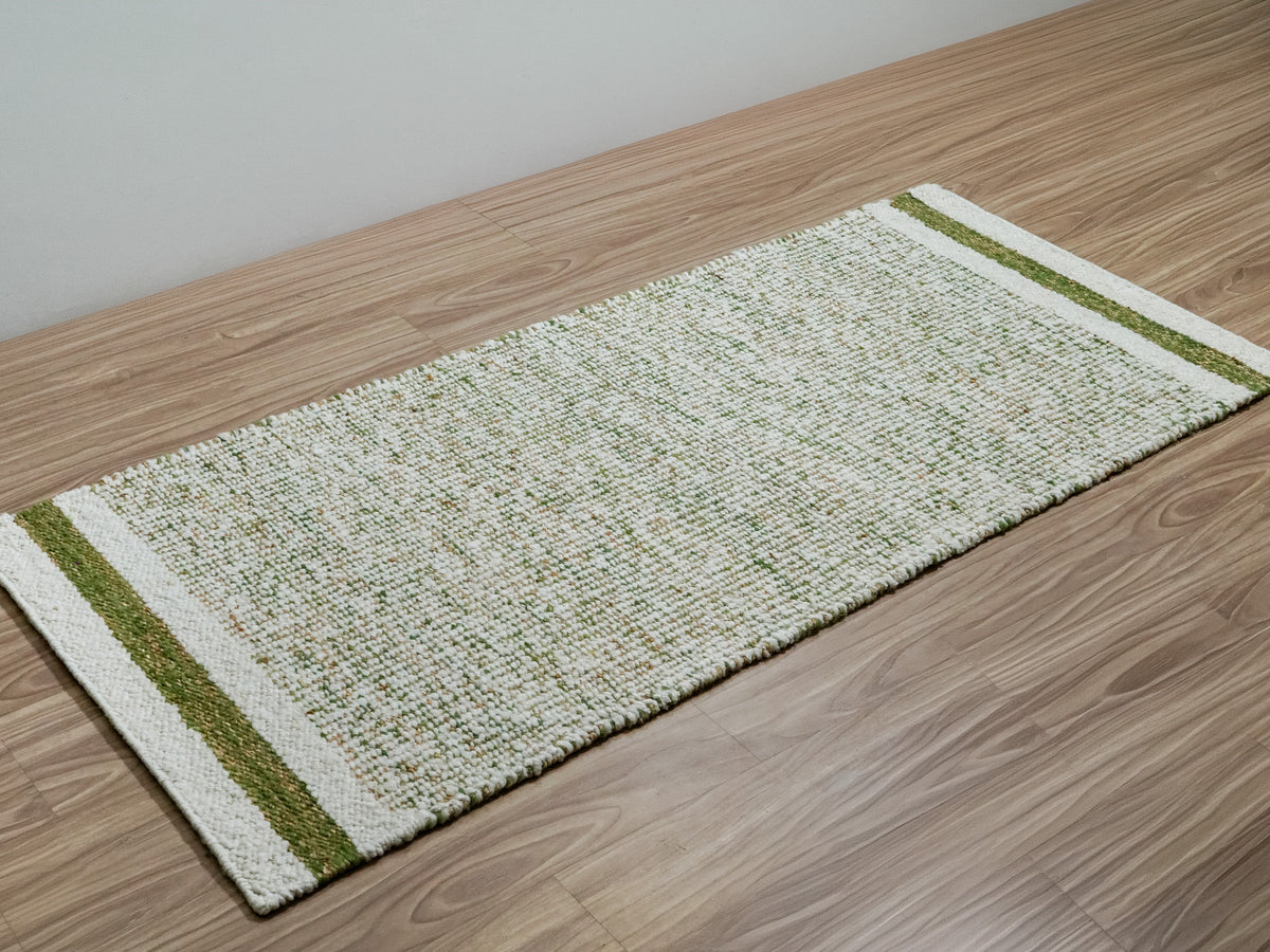 Green wool runner viewed diagonally along a wood floor beside a plain wall, with both striped ends visible.