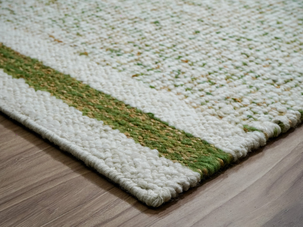 Close-up of a green wool rug corner showing a green and tan stripe between ivory bands.