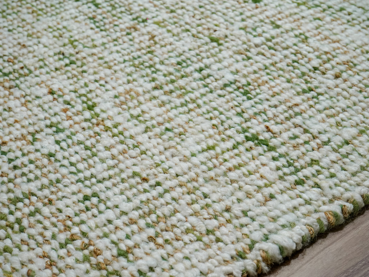 Close-up of the green wool rug's weave, textured surface and wrapped edge, with ivory and tan yarn details.