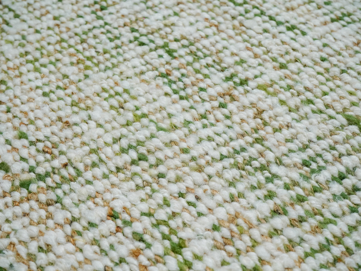 Macro view of the green wool rug's textured surface, with rounded ivory yarns interspersed with green and tan strands.