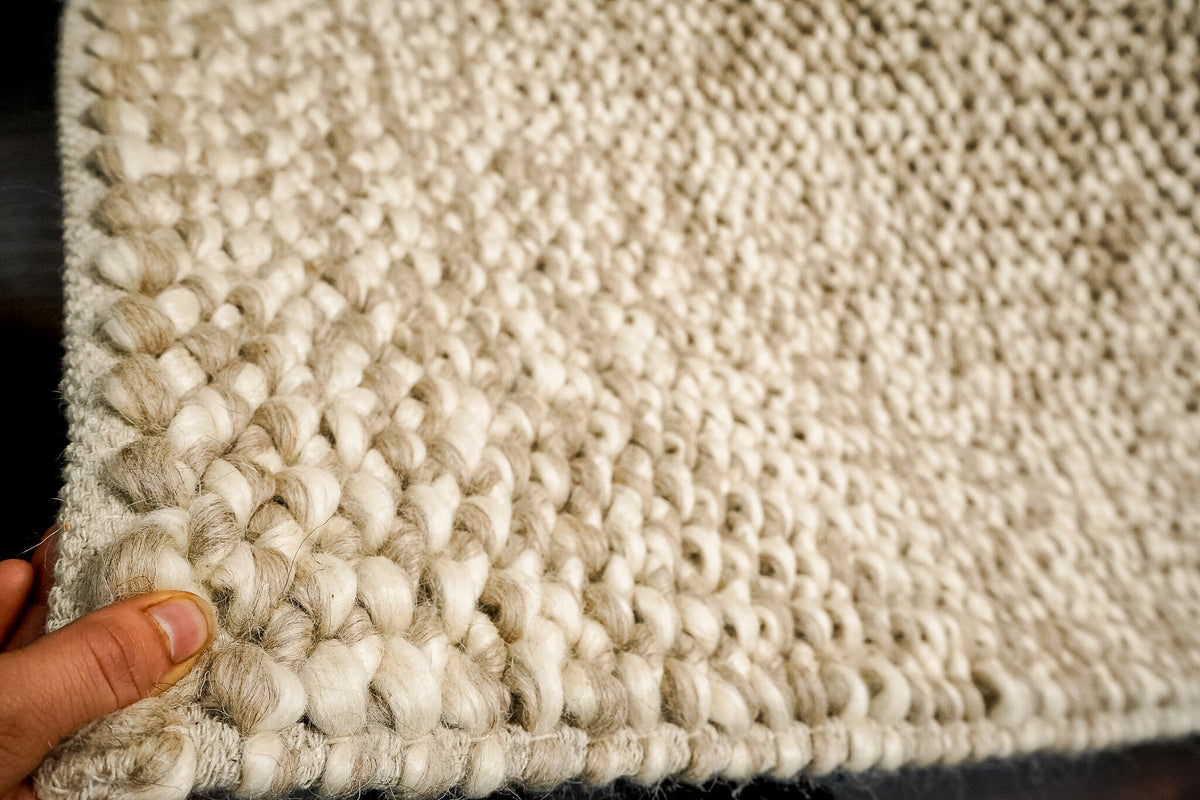 Taupe wool rug styled in a neutral bedroom
