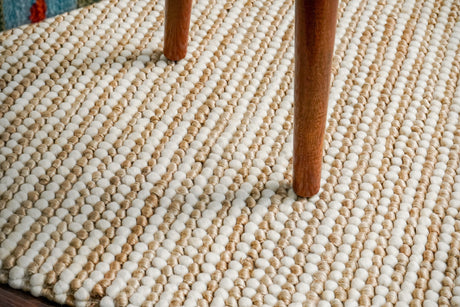 May include: Close-up view of a textured rug with a striped pattern in beige and off-white. The rug is made of small, round, looped yarn creating a nubby texture.  Two wooden chair legs are visible on the rug's surface, showcasing its durability and suitability for high-traffic areas. The rug's color palette is neutral and earthy, making it a versatile addition to various home decor styles.