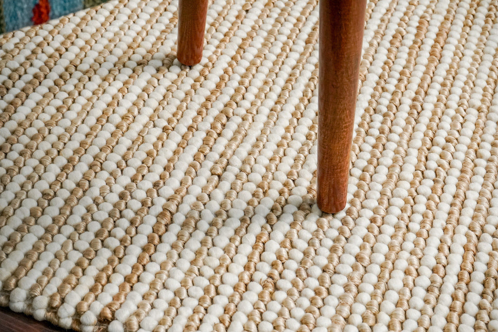 May include: Close-up view of a textured rug with a striped pattern in beige and off-white. The rug is made of small, round, looped yarn creating a nubby texture.  Two wooden chair legs are visible on the rug&#39;s surface, showcasing its durability and suitability for high-traffic areas. The rug&#39;s color palette is neutral and earthy, making it a versatile addition to various home decor styles.